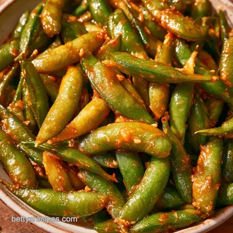 Bright green soy pods arranged in a minimalist white bowl, garnished with fresh sliced scallions and chili flakes.