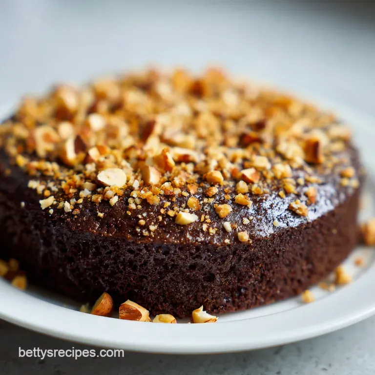 Moist, velvety mocha-colored cake slice on a white plate, paired with a dollop of whipped cream and a hazelnut.