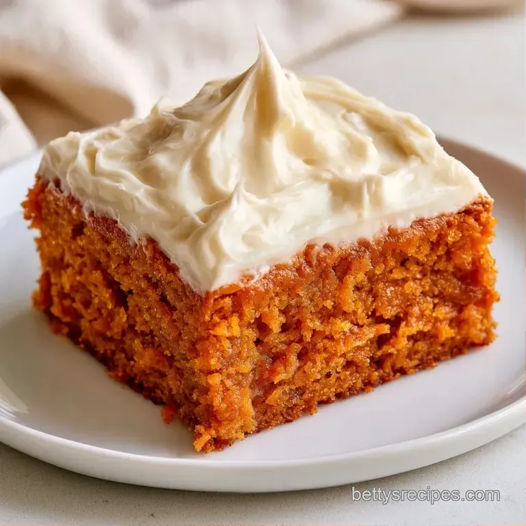 A single square of spiced orange cake topped with a swirl of white icing and a dusting of cinnamon on a white plate.