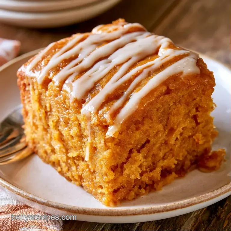 A slice of moist, orange-toned cake with a textured cinnamon crumble served on a minimal white ceramic plate.
